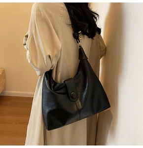 Close-up of a large black leather tote bag worn as a crossbody with beige trench coat