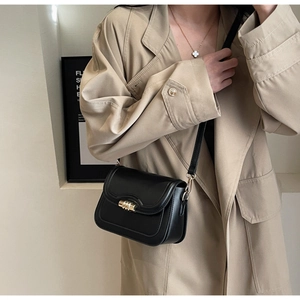 Detail of a chic black leather saddle bag with gold cylinder buckle on a model in a trench coat