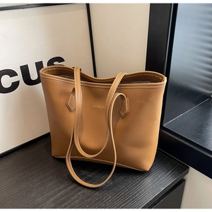 Détail d'un cabas en cuir marron avec coutures blanches et logo embossé sur bois