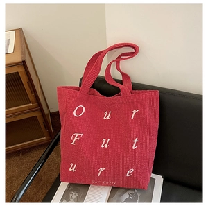 Macro view of red corduroy tote bag with Our Future text on a leather chair