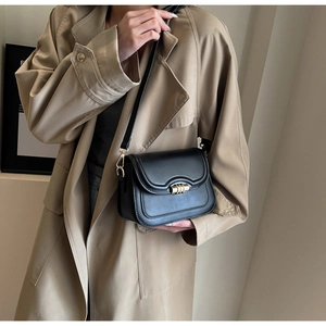 Detailed view of black saddle bag with designer gold cylindrical lock on khaki trench coat