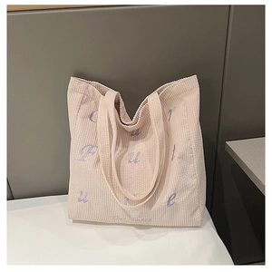 Detail of pink corduroy tote bag showing purple embroidered letters and ribbed texture