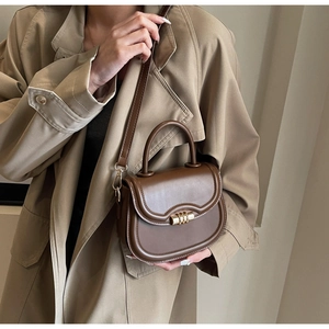 Brown retro saddle bag with gold lock buckle shown on model wearing beige trench coat