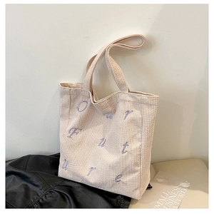 Detailed view of cream corduroy tote bag featuring purple OUR FUTURE embroidery