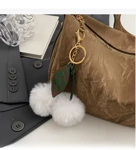 Détail du pompon en fausse fourrure blanche avec feuille verte sur un sac marron