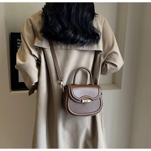 Rear view of model wearing a brown saddle bag with gold metal buckle and leather strap