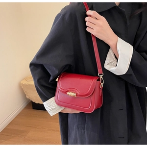 Detail of red leather crossbody saddle bag with gold metal twist lock on black coat
