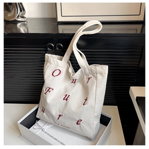 Close-up of white corduroy tote bag with red Our future embroidery in a gift box