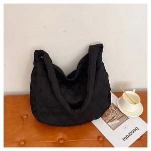 Detail of black quilted tote bag texture and wide strap on a leather bench