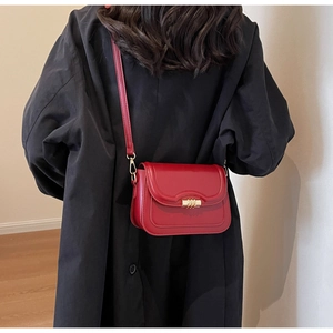 Chic red leather crossbody saddle bag with gold metal lock worn over a black winter coat
