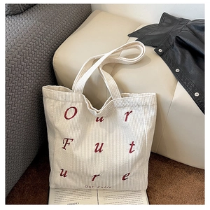 Detail of beige corduroy tote bag featuring red Our Future embroidery on fabric