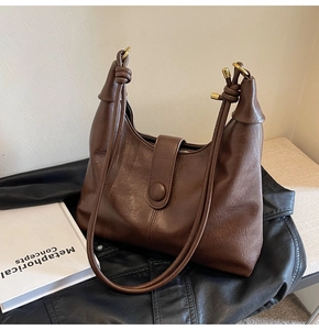 Detail of dark brown leather tote with textured lychee grain and decorative round clasp
