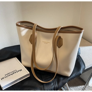 Détail d'un grand sac cabas beige avec bordure marron posé sur une veste en cuir