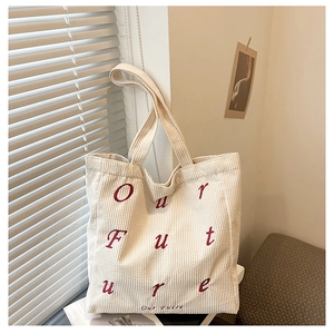 Detail of cream corduroy tote bag with red Our Future embroidery in a cozy setting