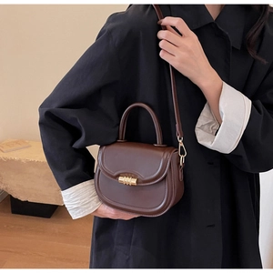Detail view of dark brown leather saddle bag with vintage gold metal buckle and hand strap