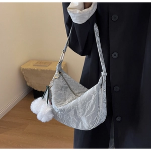 Détail du sac hobo plissé gris argenté avec pompon en peluche et ruban sur manteau noir