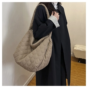 Detail of khaki quilted tote bag featuring wave stitching and side zipper on a model