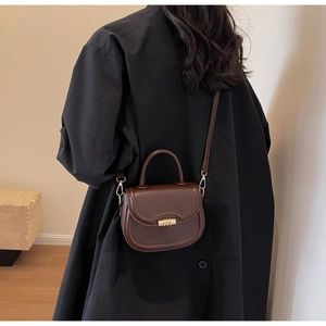 Deep brown retro saddle bag with gold metal clasp shown on model in a minimalist room