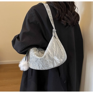 Détail du sac bandoulière argenté en demi-lune avec texture plissée et pompon blanc doux