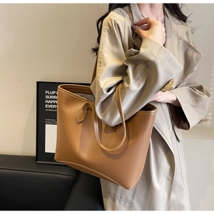 Détail d'un sac cabas en cuir marron avec surpiqûres blanches porté avec un trench-coat