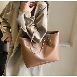 Détail d'un sac cabas en cuir marron avec lettrage doré porté par un mannequin en trench