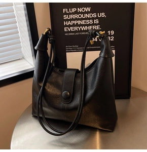 Close-up of black leather tote bag featuring golden metal ring and pleated detail