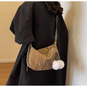 Détail du sac hobo plissé métallisé avec pendentifs en peluche blanche sur un manteau