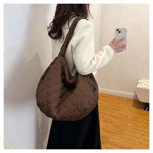 Brown quilted half-moon tote bag shown on shoulder in a minimalist indoor setting