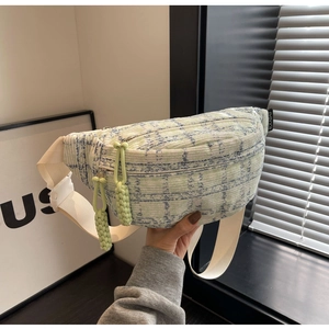 Detail of light green plaid waist bag featuring woven rope zippers and logo tag