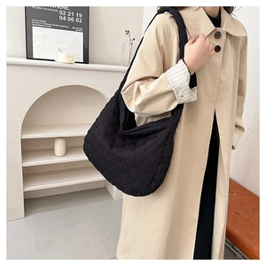 Close-up of black quilted shoulder bag with wave pattern and wide strap on a model
