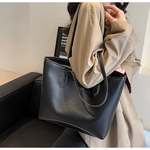 Modèle portant un grand sac cabas en cuir noir mat avec lettrage doré et surpiqûres