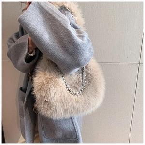 Gros plan du sac seau beige en fausse fourrure avec bandoulière chaîne sur manteau bleu