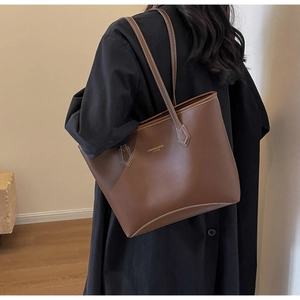 Détail d'un grand sac cabas en cuir marron avec surpiqûres blanches et logo doré