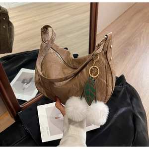 Détail d'un sac hobo en cuir marron texturé avec pendentif feuille et pompons blancs