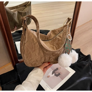 Détail d'un sac hobo marron en forme de croissant avec breloques feuilles et pompons