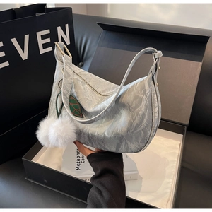 Détail du sac hobo plissé argenté avec pompons blancs et étiquette en forme de feuille