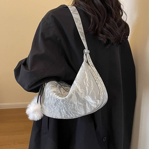 Sac hobo plissé argenté avec pompon en fourrure, porté par un mannequin en manteau noir