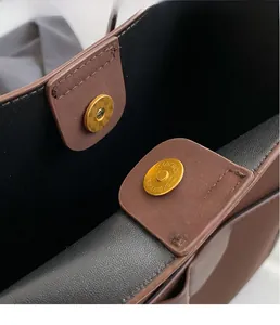 Detailed close-up of golden magnetic clasp with textured engraving on a brown tote bag