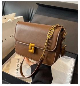 Detail view of brown leather bag with golden chain and bear charm on gift box