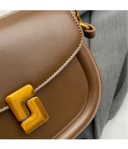 Dettaglio di borsa a sella in pelle marrone con chiusura dorata e cuciture raffinate