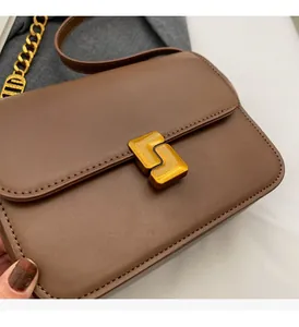 Close-up of brown leather crossbody bag with geometric gold metal buckle and chain strap