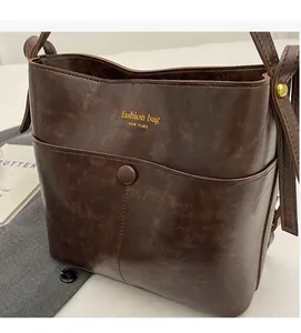 Detail of vintage brown bucket bag with gold logo, front pocket, and oily leather texture