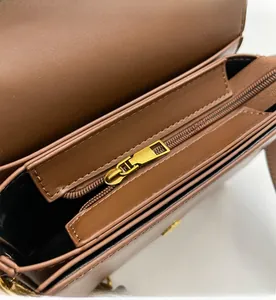 Close-up of the smooth golden metal zipper and black interior lining of a brown leather bag