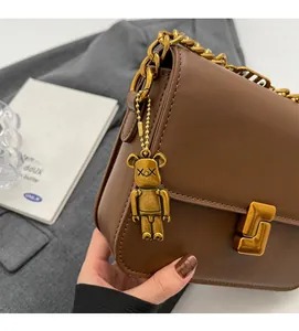 Detailed close-up of brown leather bag with golden chain and bear charm decoration