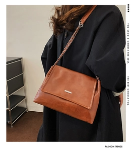 Detail view of brown caramel tote bag with silver metal bar and chain strap on black coat