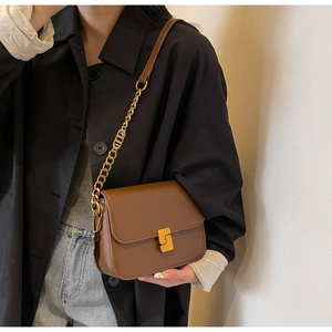 Detail of dark brown leather crossbody bag featuring gold twist lock and metal CD chain charm