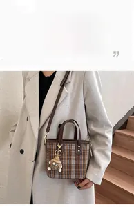 Detail view of brown plaid bucket bag with leather strap and plush monster charm accessory