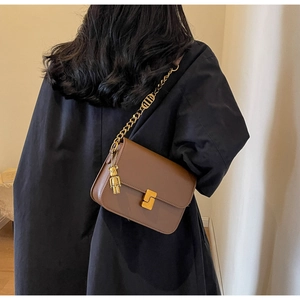 Detail view of brown vintage leather crossbody bag with gold buckle and chain strap