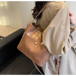Brown retro bucket bag made of oil-wax synthetic leather worn by a model in a beige trench coat