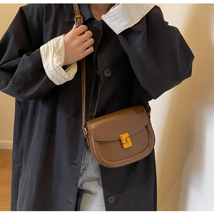 Borsa a sella in pelle marrone con chiusura dorata indossata su un trench nero